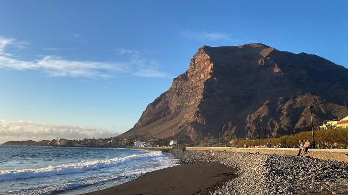 Playa de Valle Gran Rey, donde se ve la montaña, personas paseando y la avenida del paseo marítimo