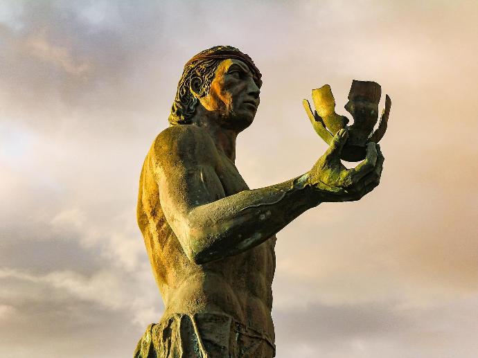 Estatua de bronce del aborigen Hautacuperche que brilla con el sol, se ve al hombre agarrando un objeto y posando con el brazo